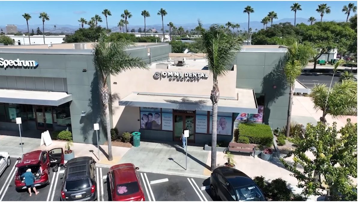 Exterior of the office building from above, with the Omni Dental Specialty sign over the entrance, palm trees and a parking lot in front