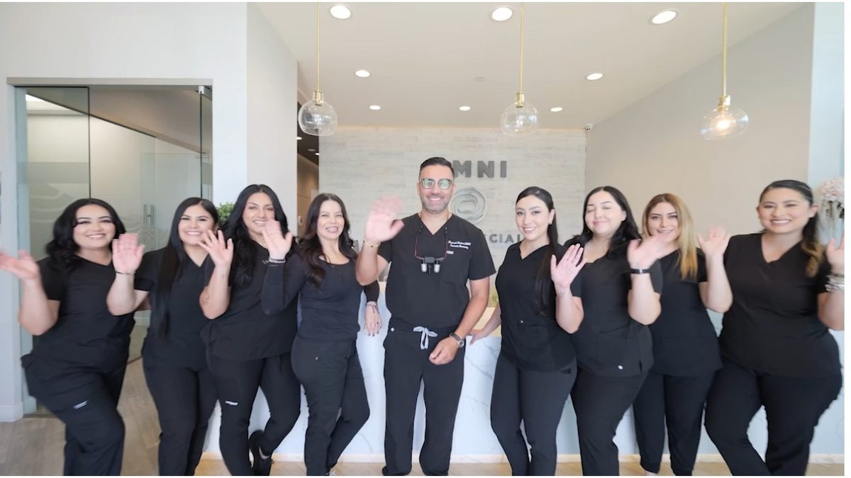 A group of people in black scrubs standing and waving in front of a reception desk