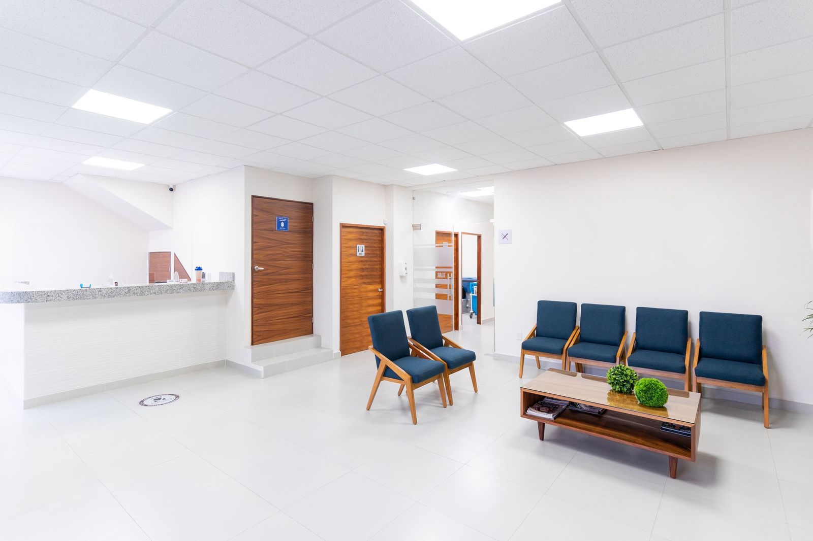 Bright dental waiting area with blue chairs, a wood coffee table and a reception counter